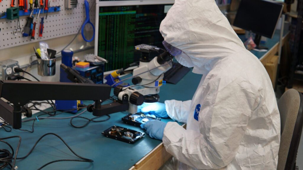 Technician in a clean suit performing data recovery and hard drive repair with a microscope